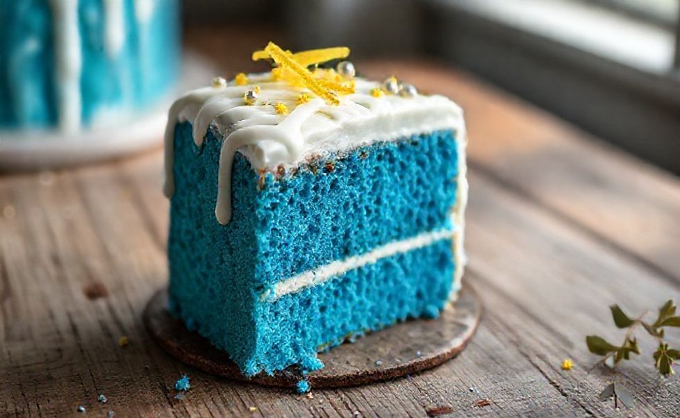 Fatia de Bolo Azul com massa úmida e vibrante, decorada com glacê branco e raspas de limão sobre mesa rústica