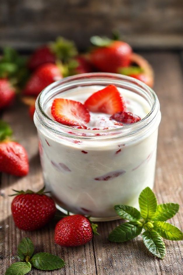 Iogurte de morango caseiro cremoso em pote de vidro com pedaços de morango visíveis, decorado com frutas frescas e hortelã