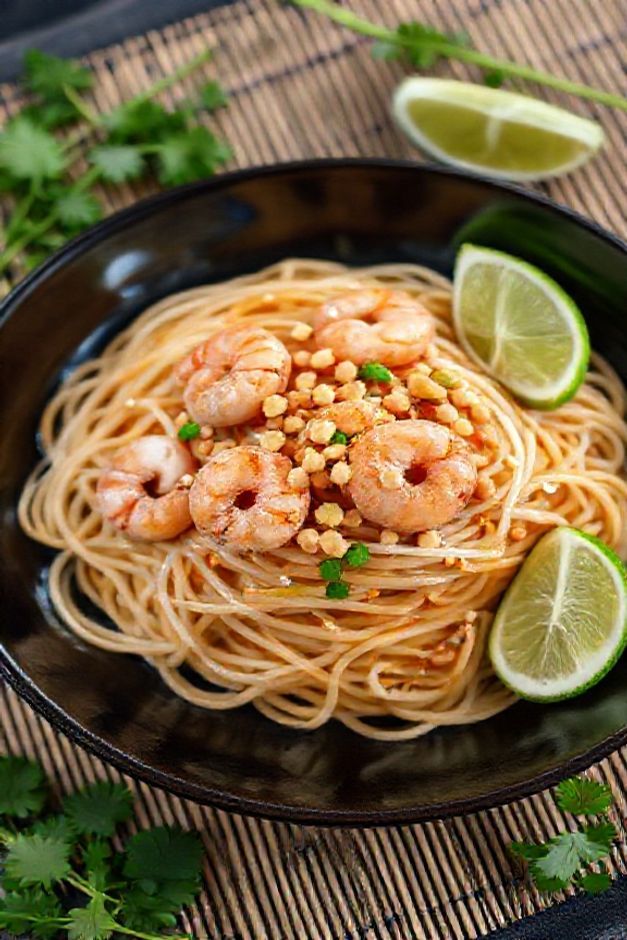 Pad thai near me servido em prato escuro com camarões, amendoim crocante, broto de feijão e limão, textura brilhante do molho tailandês