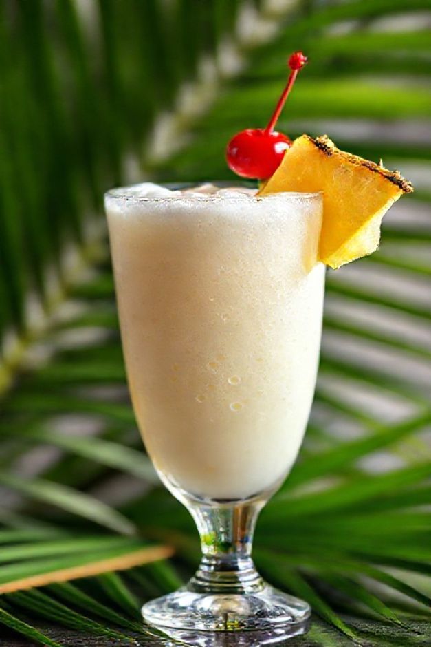 Pina colada receita servida em copo alto com decoração de abacaxi e cereja, textura cremosa e gelada com gotas de condensação