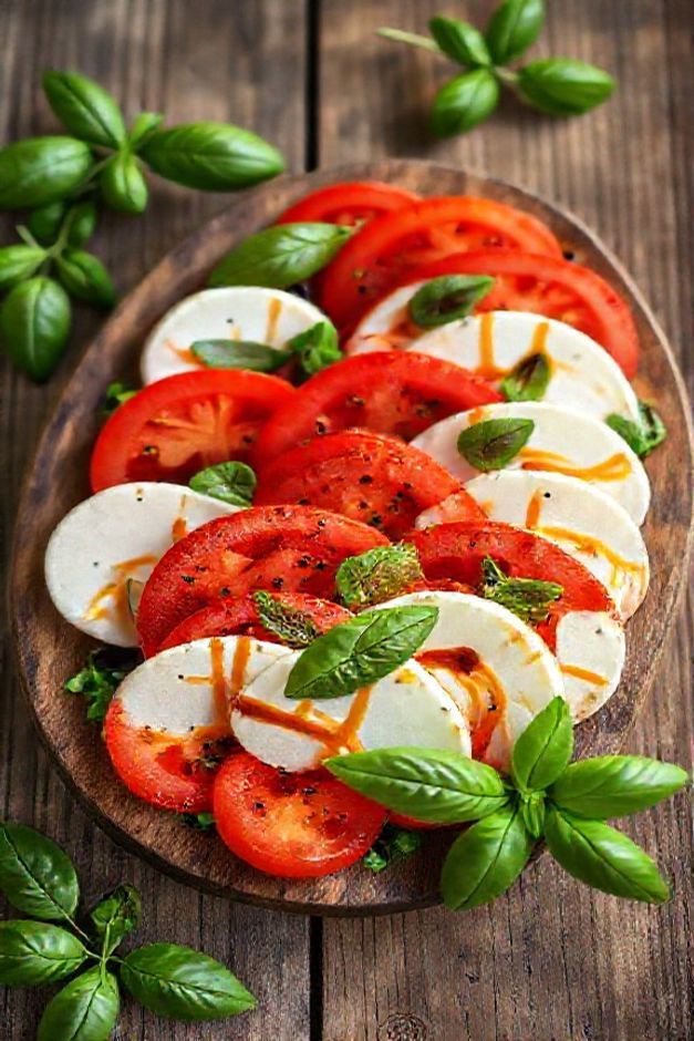 Salada caprese ingredientes dispostos artisticamente com tomates vermelhos, mozzarella branca e manjericão fresco regados com azeite